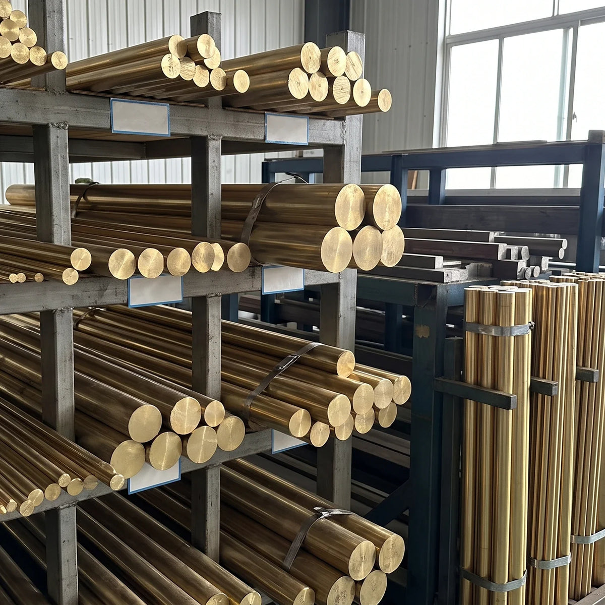 Raw brass rods and bars stacked on racks in a metalworking workshop. General material reference; not this product configuration.